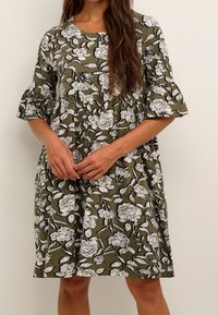 Blumendruckkleid in Olivgrün mit weißen Blumen, kurzen ausgestellten Ärmeln und einem lockeren, knielangen Design. Weiche Stoffstruktur.