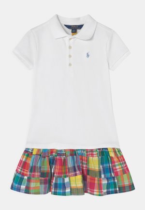 Abito polo bianco con collo a camicia e una gonna scozzese colorata caratterizzata da quadrati rossi, verdi, gialli e blu.