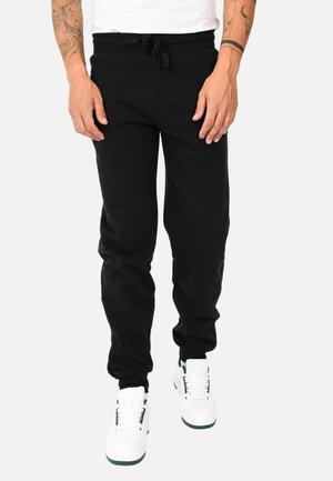 Pantaloni sportivi neri con vita elastica e cordino regolabile, caratterizzati da una vestibilità comoda e caviglie elastiche, abbinati a sneakers bianche.