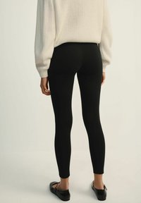 Czarne legginsy wykonane z elastycznego materiału, charakteryzujące się gładką strukturą i dopasowanym krojem. Połączone z białym, fakturowanym, oversizowym swetrem.