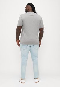 Szara koszulka z krótkim rękawem noszona z jasnoniebieskimi dżinsami i białymi trampkami, z okrągłym dekoltem i luźnym krojem.