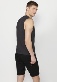 Svart ärmlös skjorta med rund hals, i kombination med svarta shorts med uppvikt ärm. Slät bomullstextur, enkel design, inga synliga mönster eller logotyper.