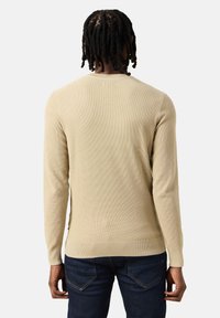 Maglione beige a maniche lunghe con un motivo a maglia testurizzato, caratterizzato da un collo rotondo e una vestibilità slim. Abbinato a jeans in denim scuro.