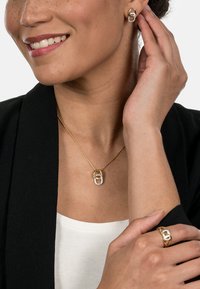 Gold-tone jewelry set featuring a pendant necklace and earrings with clear stone accents. Smooth finish with a modern design and oval shapes.