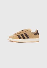 Suede sneakers in light tan with dark brown stripes. Features round laces, reinforced heel, and a white rubber sole. Brand name visible.