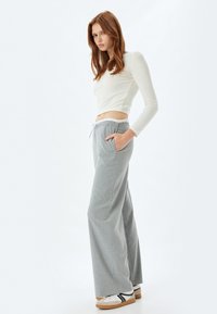 Lichtgrijze wijde broek met subtiele streepjes, elastische tailleband en zijzakken, gecombineerd met een wit aansluitend langemouwen shirt.