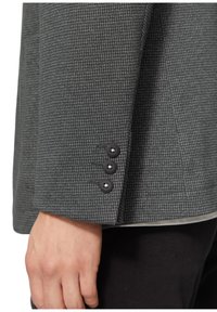 Szary blazer z teksturowanym wzorem. Posiada trzy czarne guziki przy mankietach z błyszczącym akcentem. Dopasowany krój, elegancki design.