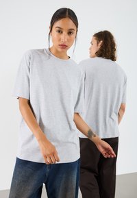 Gray cotton t-shirt with a relaxed fit, round neckline, and short sleeves, featured on two models. One model wears dark jeans.