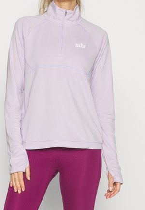 Femme portant un pull Nike violet clair avec une fermeture éclair au quart et des manches longues, associé à un legging violet foncé ajusté.