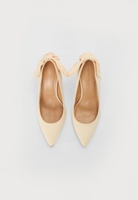 Scarpe col tacco beige con punta affilata e morbido dettaglio a fiocco alla caviglia. Realizzate in materiale liscio con una soletta chiara in contrasto.