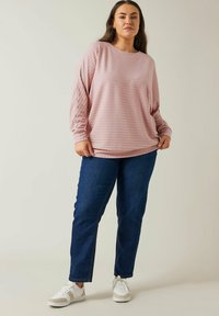 Helles rosa gestreiftes Langarmshirt kombiniert mit blauen geraden Jeans und weißen Sneakers. Der Stoff ist weich und strukturiert.