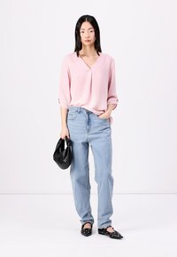 Lys rosa, teksturert bluse med V-hals; lys blå, løstsittende denimjeans; svart veske og spisse leiligheter med sølvdetaljer.