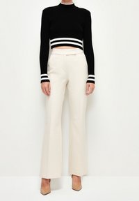 Un pull cropped côtelé noir avec des rayures blanches au niveau de l'ourlet et des poignets, associé à un pantalon large crème et des chaussures à talons nude.