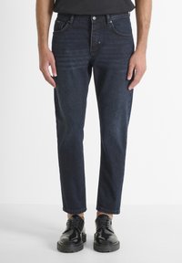 Jeans de mezclilla azul oscuro con corte recto, cinco bolsillos y un ligero desgaste. Combinados con zapatos de cuero negros con cordones para un contraste.