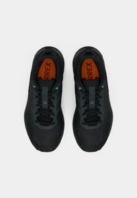 Μαύρα αθλητικά παπούτσια με υφασμάτινο επάνω μέρος με υφή, που διαθέτουν σκοτεινό γκρι λογότυπο, πορτοκαλί πάτο και μαύρα κορδόνια. Σχεδιασμένα για υπαίθρια χρήση.