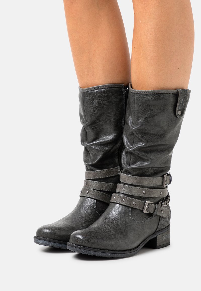 Bottes en cuir grises, décontractées, avec un bout rond, rehaussées de deux sangles cloutées et d'un petit détail en chaîne sur le talon. Talon bloc.
