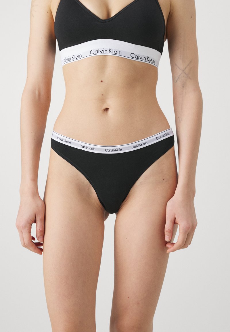 Czarne bawełniane majtki z białą elastyczną taśmą z logo "Calvin Klein". Design ma klasyczny fason stringów.