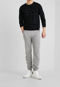 Svart långärmad tröja med texturerad lettering, matchad med ljusgrå smalpassande sweatpants med sidofickor och elastiska manschetter, bära med vita sneakers.