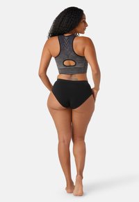 Sostén deportivo de color gris oscuro con rayas texturizadas y diseño de espalda con forma de llave, combinado con pantalones cortos negros de cintura alta, con tejido suave y curvas.