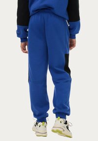 Blå sweatpants med en avslappnad passform, med svarta sidopaneler och ribbade manschetter. Kombinerat med vita och svarta sneakers med neonaccent.
