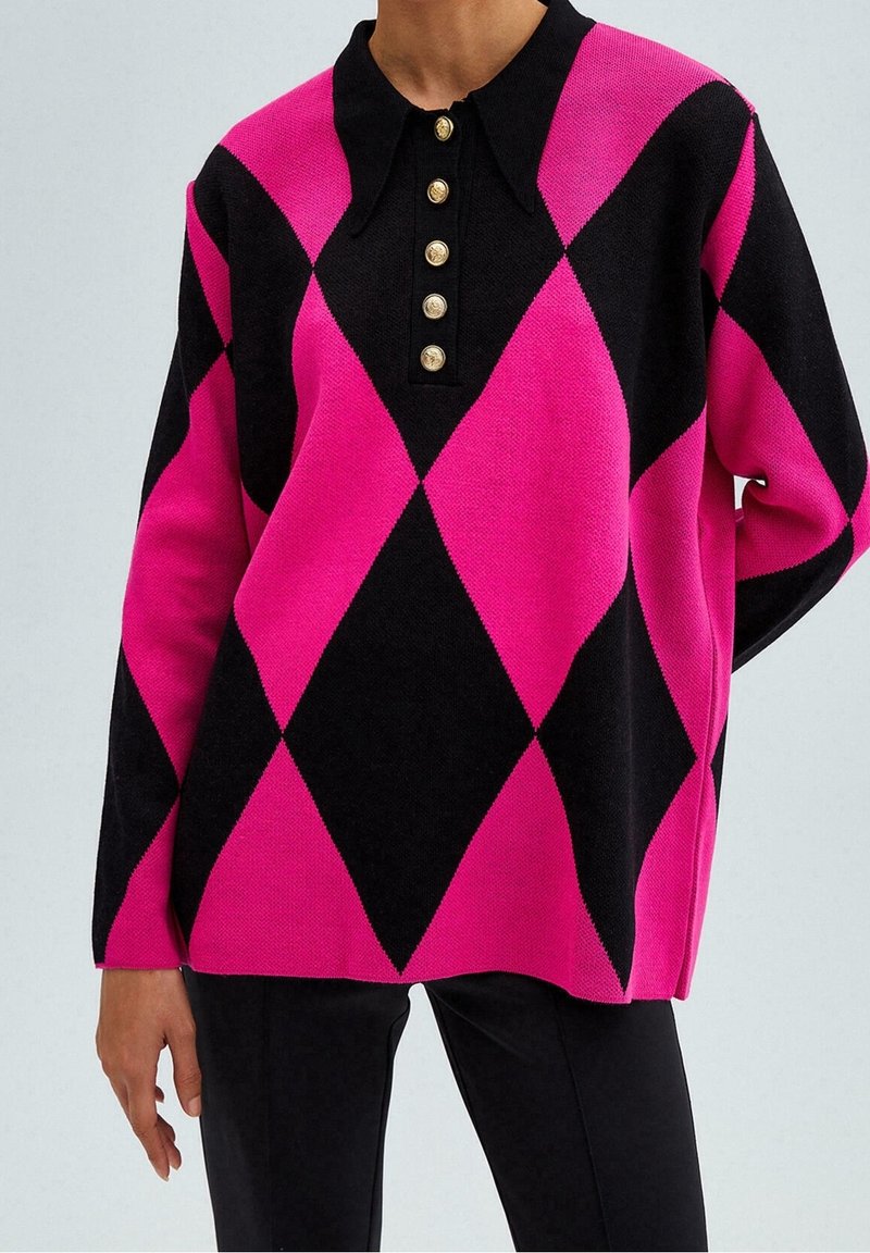 Gestrickter Pullover mit einem schwarz-pinken Rautenmuster, einem spitzen Kragen und goldenen Knöpfen, die sich vorne entlangziehen. Leicht übergroße Passform.