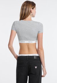 T-shirt gris crop avec des manches courtes, présentant un bandeau de marque blanc à l'ourlet, associé à un jean noir taille haute avec des poches visibles.