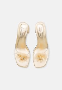 Sandales à glissière transparentes avec une finition métallique dorée, des embellissements floraux avec des accents dorés et un petit talon carré.