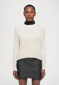 Crème ribgebreide trui met ronde hals, gecombineerd met een donkergrijze rok met twee voorzakken. Beide kledingstukken hebben een gestructureerde pasvorm.