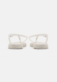 White flip-flops with narrow straps and textured, braided soles. The design is minimal with no embellishments or patterns.