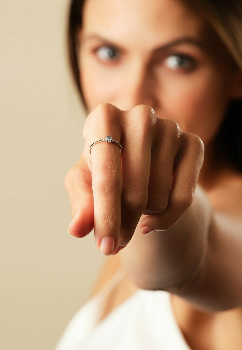 Silverring med en delikat band och en liten blå sten, bärs på ett finger som pekar framåt. Slät yta och minimalistisk design.