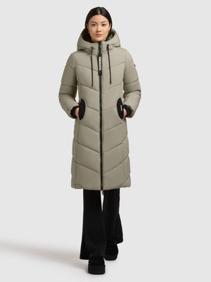 Beige pufferjack met een capuchon, voorzien van een ritssluiting aan de voorkant, zwarte accenten op de zakken en een gestikte design. Draagt over zwarte flared broek.