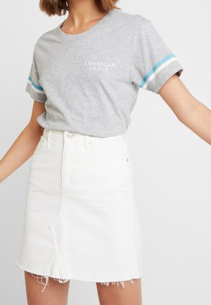 Woman wearing a grey American Eagle t-shirt with blue and white sleeve stripes and a white denim skirt with frayed hem.