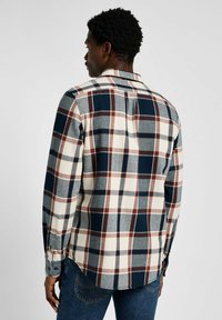 Camicia di flanella a quadri nei colori blu navy, rosso e crema. Maniche lunghe, polsini con bottoni e dettaglio nella parte posteriore. Tessuto morbido e texture con vestibilità casual.