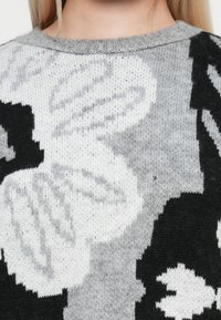 Maglione lavorato a maglia con un motivo floreale in bianco, nero e grigio. Tessuto morbido con scollatura rotonda e vestibilità ampia.