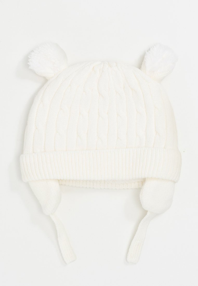 Cappello bianco lavorato a maglia con orlo a costine, dotato di due pompon sulla parte superiore e orecchie con lacci per una vestibilità sicura. Design a trecce in rilievo.