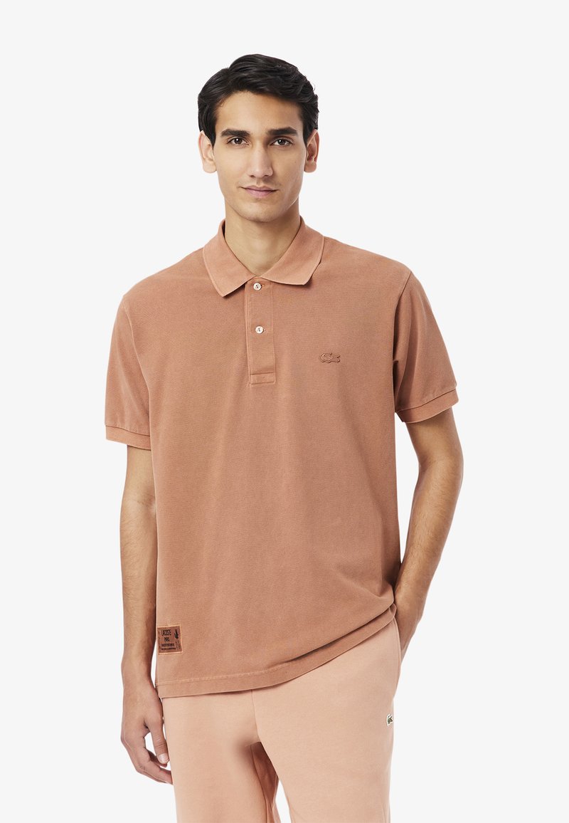 Brun bomullspolo med klassisk krage, försedd med en tre-knapps knäppning och en broderad logotyp på bröstet. Kortsleeves.