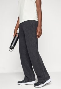 Μαύρες φόρμες με χαλαρή εφαρμογή και απαλό υλικό. Συνοδεύονται από μια μαύρη μπουκάλι νερού και αθλητικά παπούτσια με λευκές σόλες.