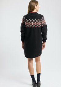 Robe en tricot noire avec un empiècement à motifs en rouge et crème. Manches longues avec des accents rouges. Texture douce et coupe longueur genoux.