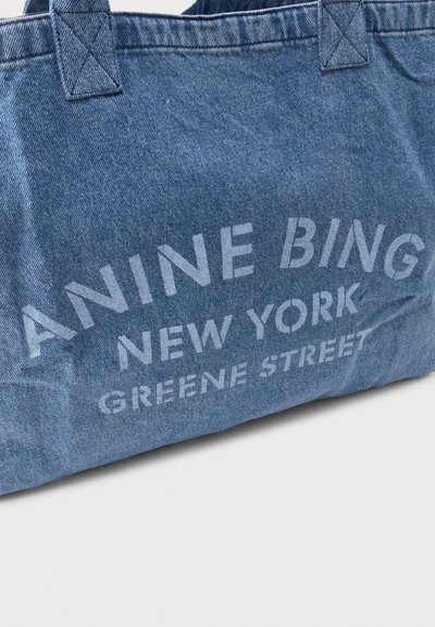 Blauwe denim draagtas met gestikte handvatten en witte tekst "ANINE BING NEW YORK GREENE STREET" aan de voorkant.