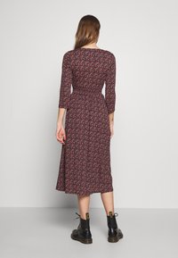 Dunkelrotes florales Midikleid mit Dreiviertelärmeln, taillierter Taille und ausgestellt Rock, kombiniert mit schwarzen Stiefeletten.