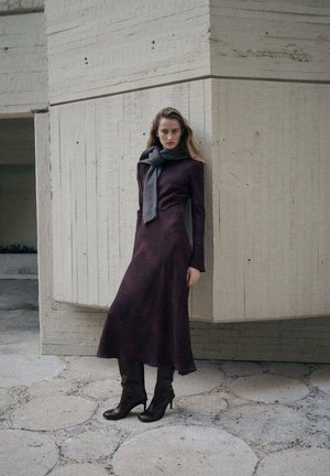 Bordeauxrode jurk met lange mouwen, een aansluitend lijfje en een vloeiende rok, gecombineerd met een grijze sjaal en bruine laarzen met hak. Stoffen afwerking met textuur.