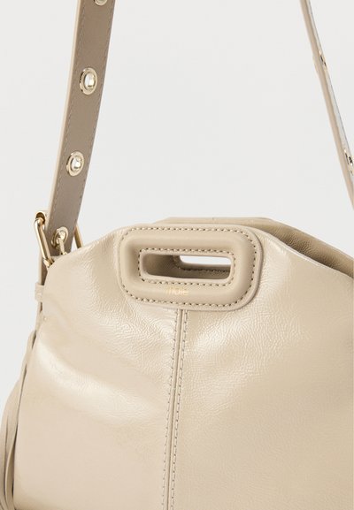 Μπεζ τσάντα χειρός από υφή σύνθετου υλικού, με χειρολαβή στο επάνω μέρος που διαθέτει ορθογώνιο άνοιγμα και αποσπώμενο λουρί με χρυσές λεπτομέρειες.