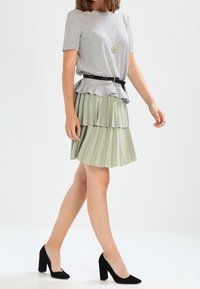 Top de rayas de manga corta con dobladillo peplum combinado con una falda plisada de color verde claro. La modelo lleva zapatos de tacón negro y un cinturón negro.