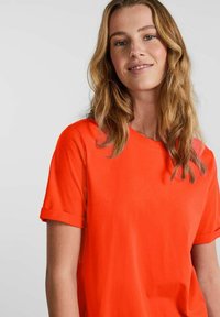 Kortærmet T-shirt i lys orange, lavet af glat bomuld, med rullemansjetter og en klassisk rund hals. Enkel design, uden mønstre.