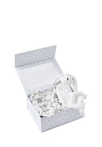 Geschenkbox mit einem weißen Einteiler mit schwarzen Blumenmustern und einem weichen weißen Hasen mit schlaffen Ohren sowie einer kuscheligen Decke.