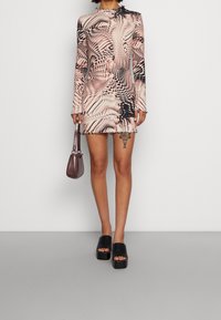 Robe mini à manches longues avec un motif abstrait rose et noir, fabriquée en tissu extensible. Présente un col volanté et une silhouette ajustée.