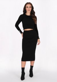 Costum format din două piese, de culoare neagră, care include un top scurt cu mâneci lungi și accente cu nasturi pe mâneci, și o fustă tip creion ajustată. Textură strălucitoare.