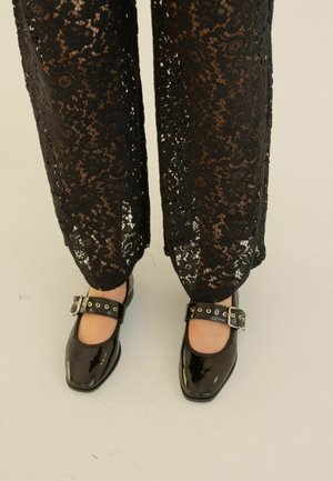 Zapatos Mary Jane de charol negro con punta redonda y una amplia correa en el tobillo que incluye herrajes de plata, combinados con pantalones de encaje negros.