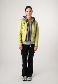 Lichtgroene leren jas met een grijze capuchon over een grijze top. Zwarte uitlopende broek en grijze sneakers completeren de outfit. Eenvoudig ontwerp, geen patronen.