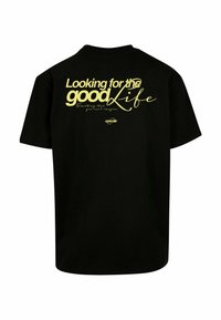 T-shirt en coton noir avec un graphisme en texte jaune bien visible au dos : "À la recherche de la belle vie" avec des accents en cursive.